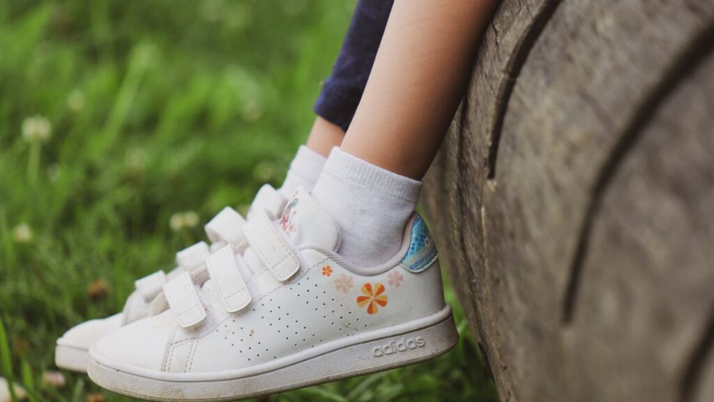 Pieds d'enfant en baskets posés sur un tronc d'arbre dans une prairie